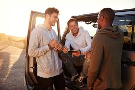 three men hanging out with smiles besides a car