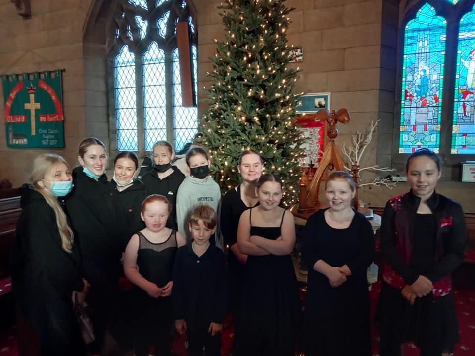 A group of women stand in a church smiling at the camera. A Christmas tree behind them.